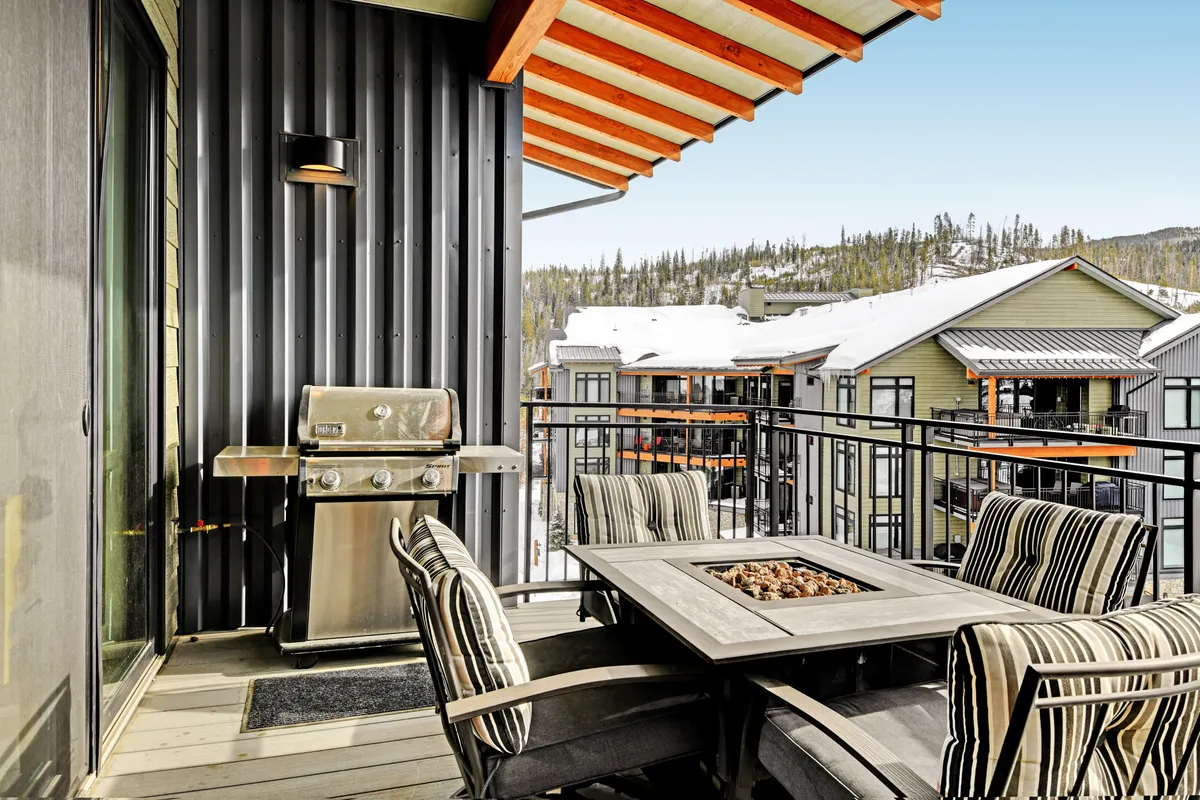 A close-up of an outdoor seating area on a balcony, featuring a BBQ grill, fire pit table, and striped chairs. The setup is casual and welcoming, ideal for alfresco dining or socializing with friends while enjoying the fresh mountain air.