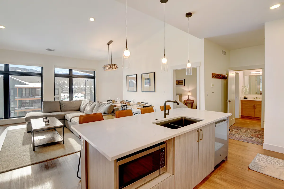 This image showcases a bright, open-concept interior with a kitchen island, sofa, large windows, and a connected dining area. The space feels modern, spacious, and welcoming, encouraging group gatherings and family activities. The large windows subtly hint at a connection with the outside world, aligning with the 'explore' section context.