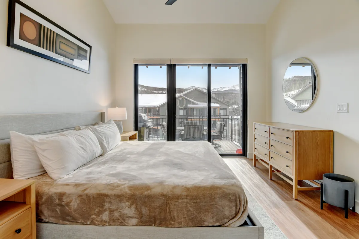 A peaceful second bedroom with a plush queen bed, window views, a dresser, and calming artwork. The mood is restful, offering a sense of quiet retreat for friends or family.