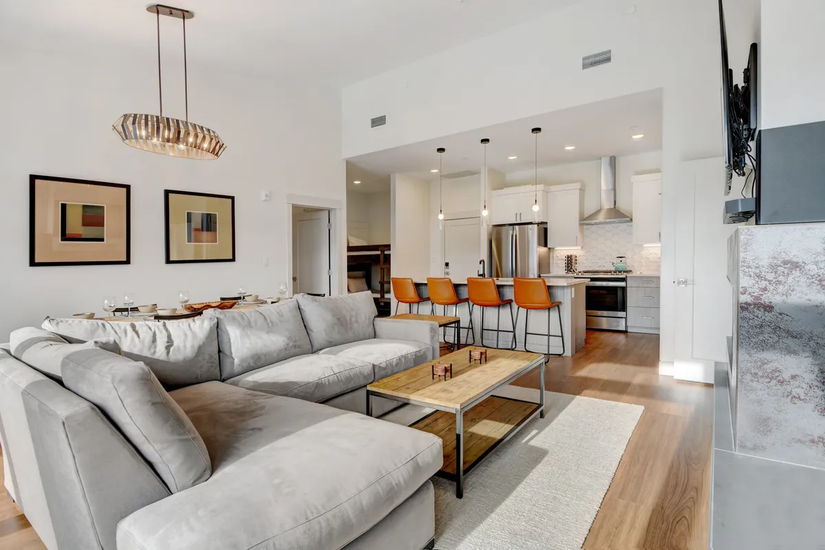This open-plan interior features a sofa, dining table, bar stools at a kitchen island, and prominent artwork. The layout is ideal for gatherings, allowing for versatile use by families or groups. The space looks clean, uncluttered, and animal-free, catering to those needing a pet-allergy-friendly environment.