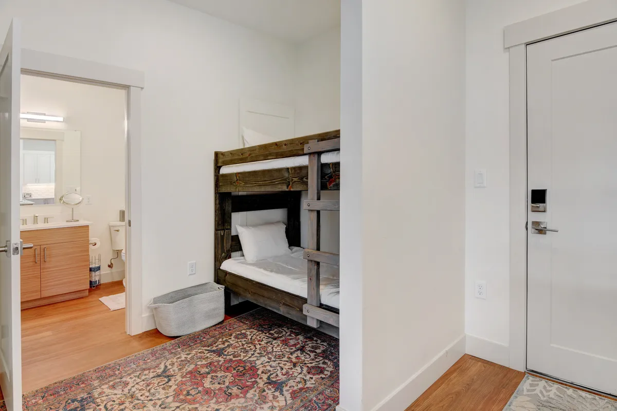 A playful and inviting bunk area featuring a sturdy bunk bed, a cozy rug, and the bathroom door nearby. The setup is child-friendly and practical, suggesting a perfect spot for young adventurers or additional guests.