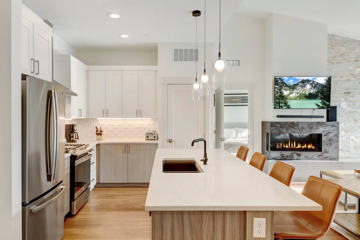 A bright, modern interior displaying a kitchen with an island, stainless steel appliances, a wall-mounted TV, and a contemporary fireplace. The layout invites both cooking and relaxation, with a family-friendly feel for entertaining or unwinding after outdoor adventures.