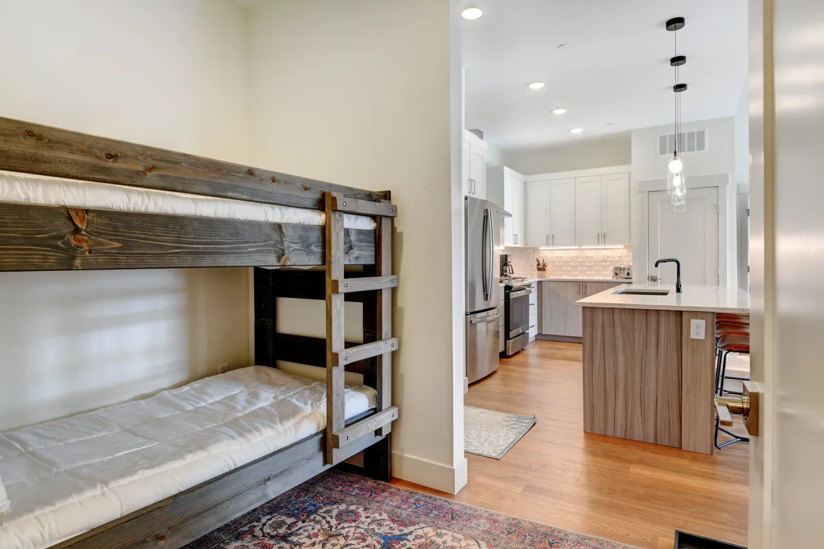 This family-friendly interior scene features a cozy bunk bed, a kitchen island for meal prep, and a decorative rug, creating an inviting environment ideal for gathering after a day of adventure.