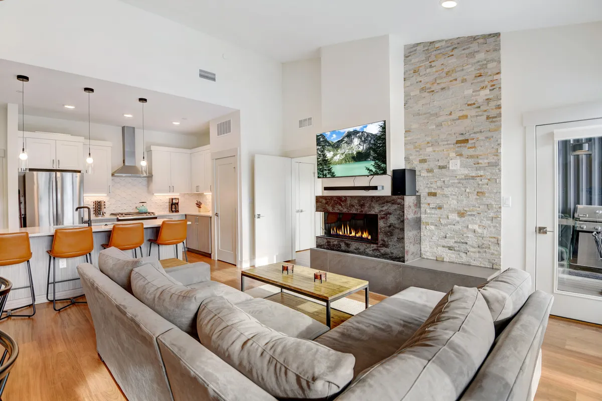 A spacious, cozy living area featuring a sofa, fireplace, kitchen island, television, and dining area. The setting is perfect for socializing, cooking, and unwinding after a day of mountain activities.