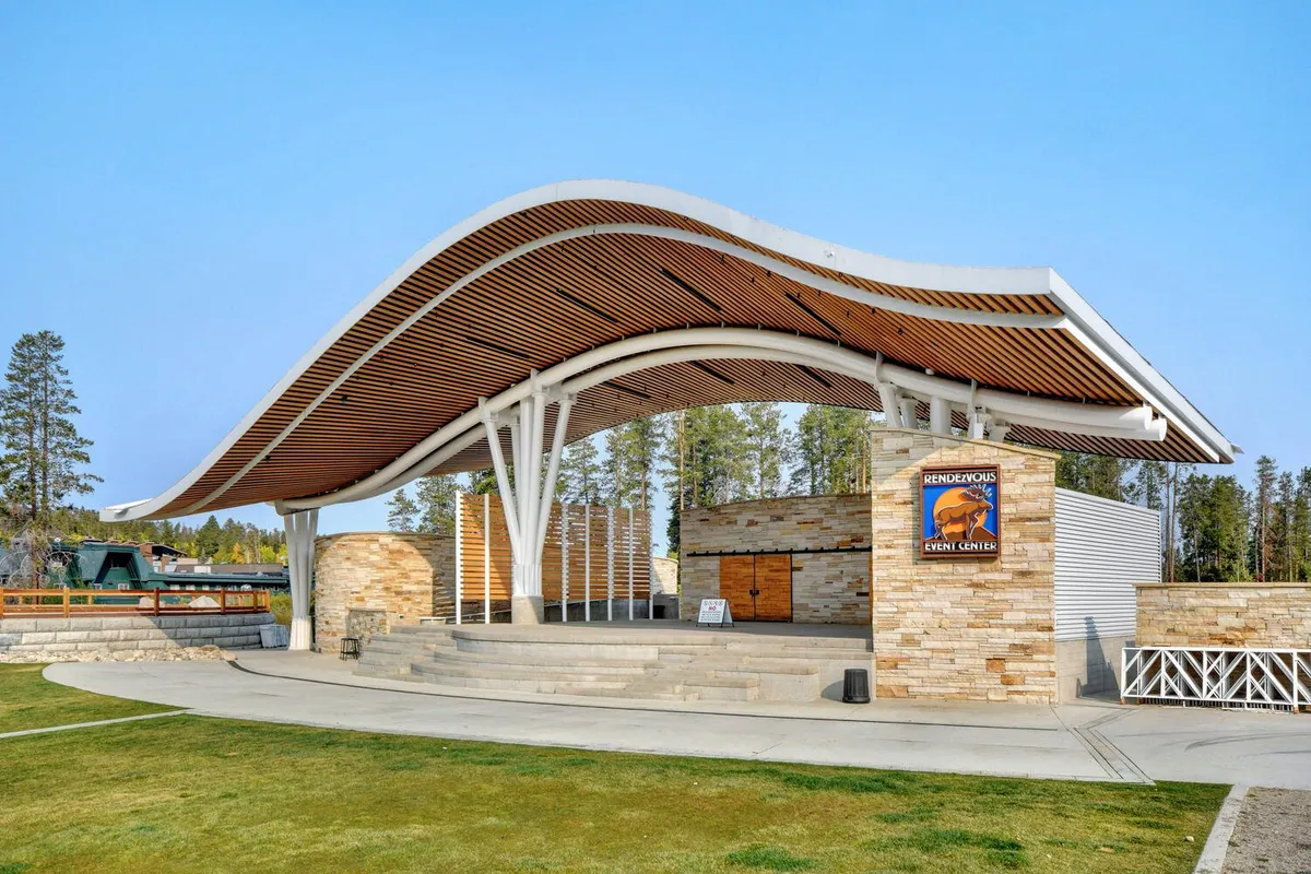 This image features the Rendezvous Events Center at Hideaway Park, with its striking curved roof structure, stone façade, and steps leading to an outdoor stage. The space is clearly designed for community gatherings, concerts, and seasonal events.